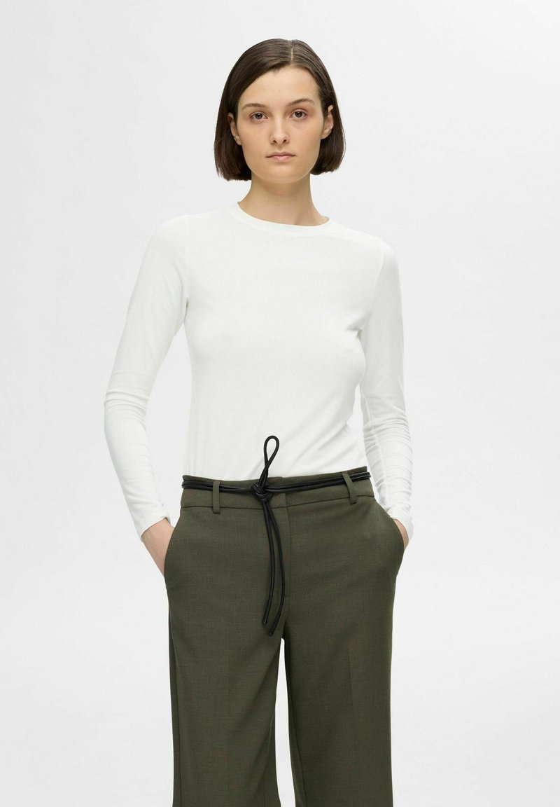 Witte langmouwen top gecombineerd met olijfgroene high-waisted broek. De broek heeft een zwarte geknoopte riem en zijzakken.