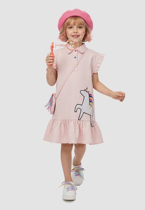 Ung pige i pink kjole med enhjørningemærke, pink baret, farverige skosnørebånd og armbånd, der blæser sæbebobler med sæbeboblepind.