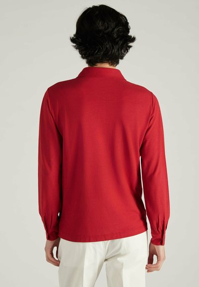 Rode longsleeve shirt met kraag, voorzien van knopenmanchetten en een gladde textuur, gecombineerd met witte broek. Achteraanzicht weergegeven.