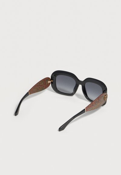 Lunettes de soleil carrées noires surdimensionnées avec des verres dégradés et des branches décoratives marron et or à motifs.