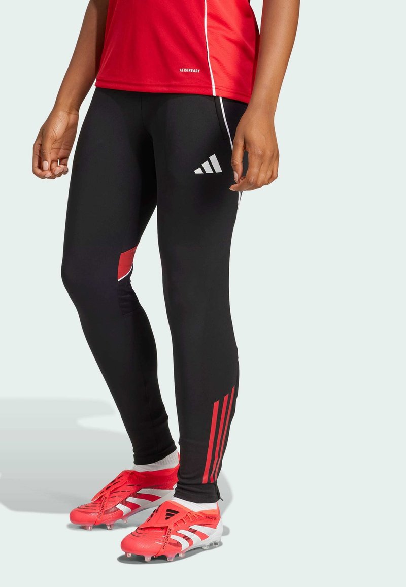 Zwarte sportleggingen met rode accenten, met aan de zijkant drie witte strepen. Draagt rode voetbalschoenen met witte details.