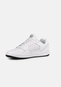Sneaker bianco con tomaia in pelle liscia, pannello laterale in rete, perforazioni per la traspirabilità e suola in gomma nera. Caratterizzato da lacci piatti.
