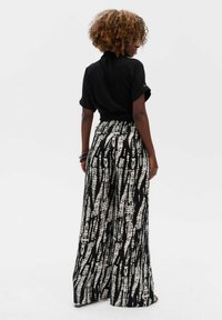 Zwart T-shirt met korte mouwen, gecombineerd met wijd aansluitende broek met een zwart en crèmekleurig abstract patroon. Zacht materiaal met een elastische tailleband.