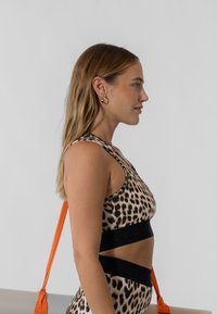 Sportska majica s leopard uzorkom i crnim elastičnim pojasom s logotipom branda, uparena s narančastom torbom za rame, od glatkog materijala, s racerback dizajnom.