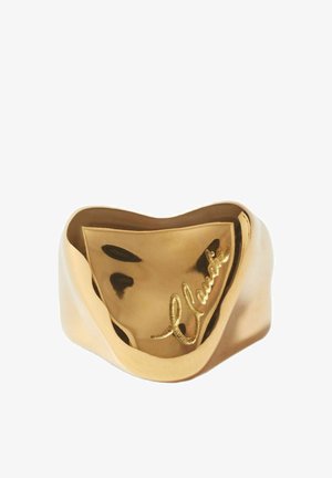 Large bague en or avec une surface ondulée et réfléchissante et une signature gravée en cursive à l'avant.