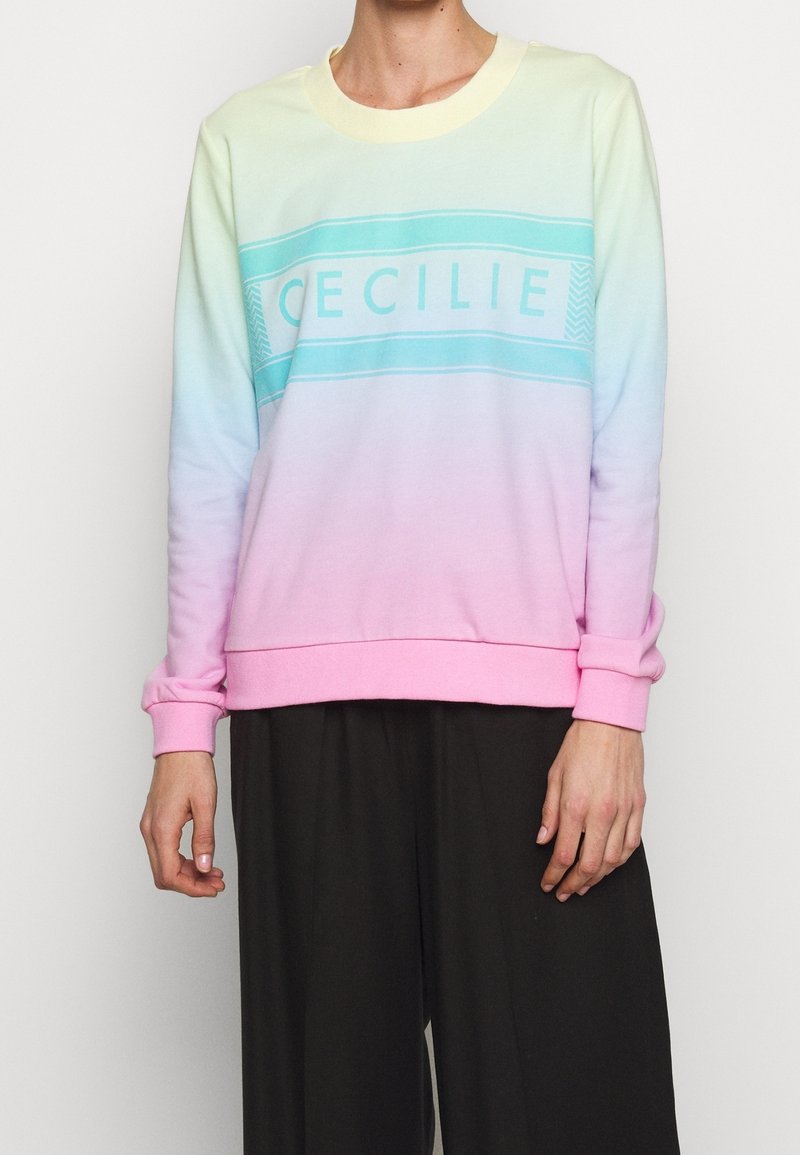 Sweatshirt med en gradientfärgskala från pastellgult till rosa, med en central blå logotyp "CECILIE" och ribbade ärmslut och nederkant.