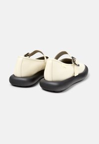 Sandalias sintéticas beige con una correa trasera y una suela de goma negra, con un hebilla decorativa y una textura suave en el cuerpo.