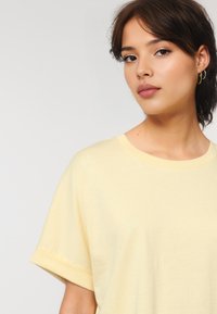 Geel t-shirt met korte mouwen, zachte katoenstof, ronde hals, relaxed fit, opgerolde mouwen, gladde textuur, geen zichtbare patronen of hardware.