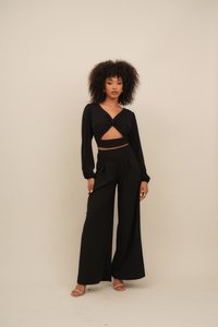 Black two-piece set featuring a long-sleeve top with a twisted cutout design and high-waisted wide-leg pants, made of a smooth fabric.