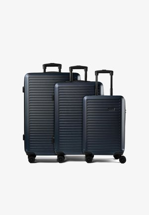 Drei dunkelblaue Hartschalenkoffer mit horizontalen Rillen, ausgefahrenen schwarzen Teleskopgriffen und vier Spinner-Rollen, nach Größe angeordnet.