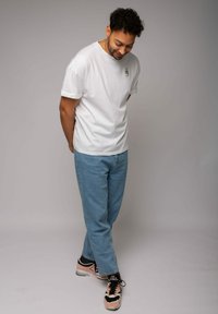 Weißes Baumwoll-T-Shirt mit aufgerollten Ärmeln, versehen mit einem kleinen grünen Logo; kombiniert mit hellblauen, lockeren Jeans und schwarz-pinken Sneakers.