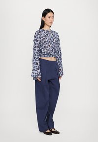 Floral-patterned, light blue cropped blouse with long sleeves, paired with high-waisted, navy blue wide-leg trousers and dark flat shoes.