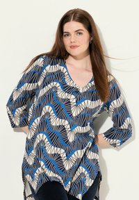 Tunique fluide avec un décolleté en V, présentant un motif de vagues marine, crème et bleu, des manches 3/4 et un ourlet asymétrique.
