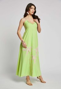 Langes, hellgrünes Kleid mit Spaghettiträgern, das mit rosaner Blumenstickerei und einem fransigen Saum versehen ist, kombiniert mit transparenten Absätzen.