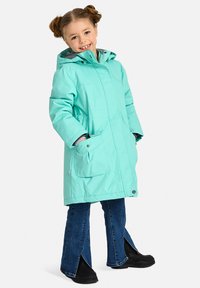 Mėtų žalios spalvos žieminė striukė su gobtuvu, dviem priekinėmis kišenėmis ir pilku pamušalu, derinama su plačiomis tamsiai mėlynomis džinsinėmis kelnėmis ir juodais batais.