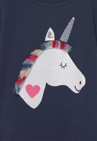 Marineblaue T-Shirt mit einem Einhorn-Design, das einen glitzernden Horn, eine farbenfrohe Fransenmähne und ein pinkes Herzdetail am Hals zeigt.