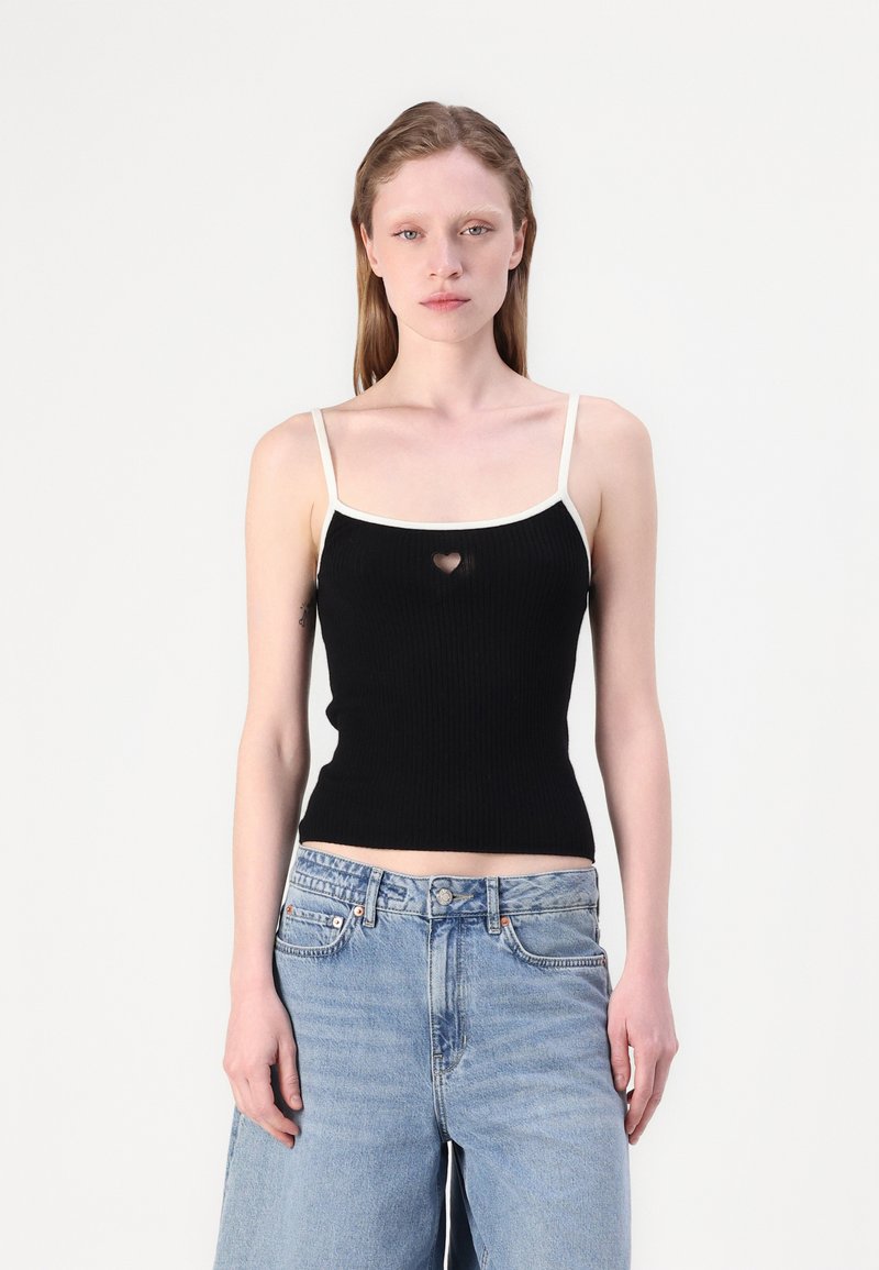 Svart ribbet tank topp med hvite stropper, med et lite hjertekutt ved brystet. Kombinert med løse lyseblå jeans.
