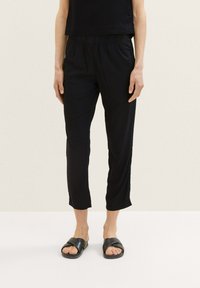 Zwarte cropped pants met een elastische tailleband, gemaakt van lichtgewicht stof, gecombineerd met zwarte platte instapsandalen.