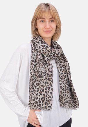 Foulard en imprimé léopard avec des tons beiges et noirs, en tissu léger aux bords effilochés, drapé élégamment sur un haut de couleur claire.