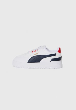 White sneaker with navy accents, red heel detail, textured sides, lace-up closure, and a thick white rubber sole. Gold logo on the side.