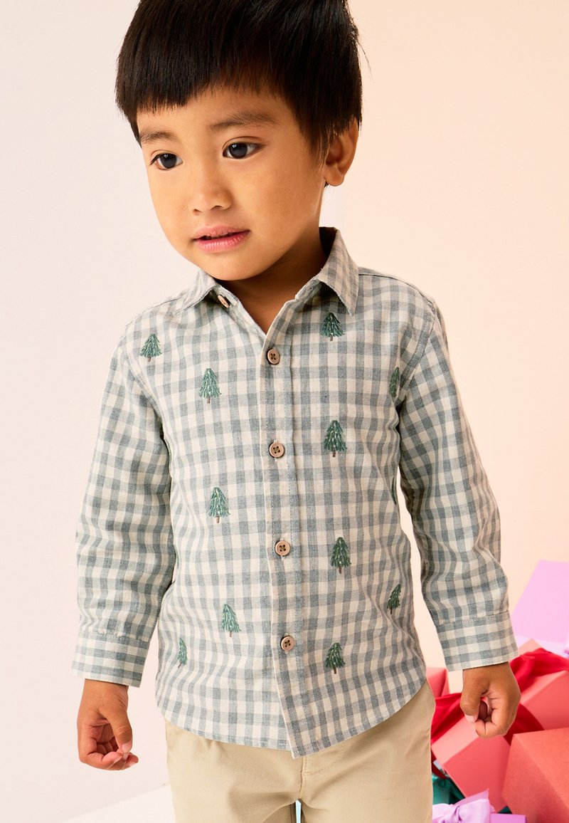 Chemise boutonnée à carreaux verts et blancs avec de petits sapins brodés, manches longues et boutons en bois. Tissu en coton.