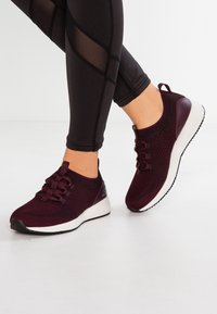 Vinröda träningsskor med överdel i stickad design, snörning och vit texturerad sula. Matchas med svarta leggings med mesh-detaljer.