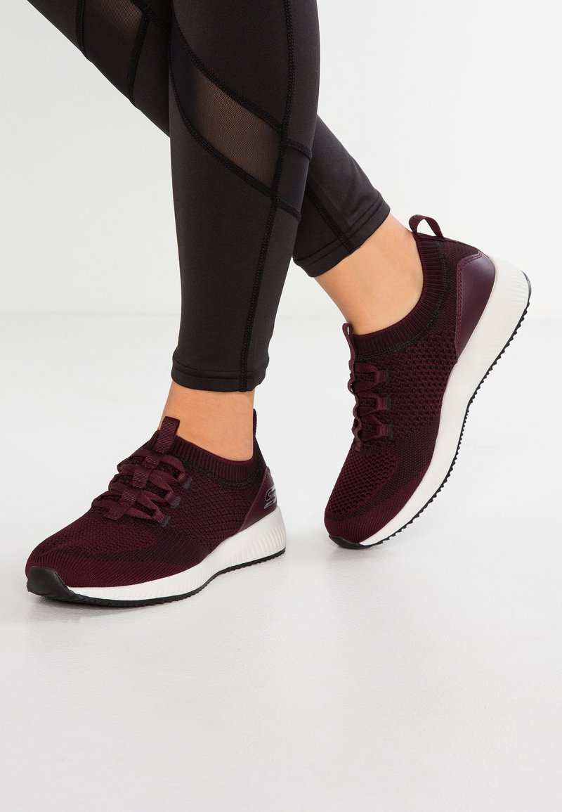 Vinröda träningsskor med överdel i stickad design, snörning och vit texturerad sula. Matchas med svarta leggings med mesh-detaljer.