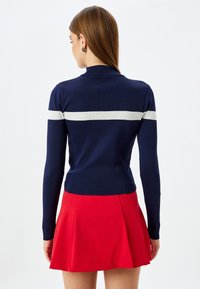 Maglietta a maniche lunghe a coste blu navy con una striscia orizzontale bianca sulle spalle, abbinata a una gonna plissettata rossa brillante. Design semplice e aderente.