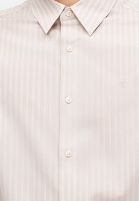 Hellbeige gestreiftes Hemd mit Knopfleiste, klassischem Kragen und dezent auf der Brust eingesticktem "cK"-Logo.