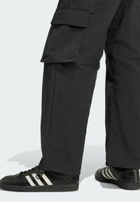 Čierne cargo nohavice vyrobené z textúrovaného materiálu s voľným strihom. Obsahujú veľké bočné vrecká a zodpovedajúci pár čiernych tenisiek s bielymi prúžkami.