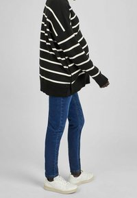 Svart och vit randig oversized tröja, blå jeans och vita sneakers. Tröjan har en ribbad nederkant och sidofickor.