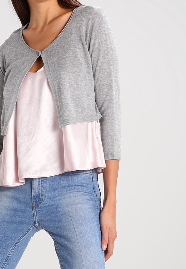Grå, stickad cardigan med trekvartsärmar, öppen fram, bärs över en pastellrosa satinblus, parat med ljusblå jeans.