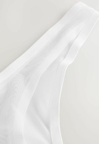 Hvid gennemsigtig stofthong med en glat bånd og tekstureret meshpanel, der fremhæver et letvægts- og åndbart design.