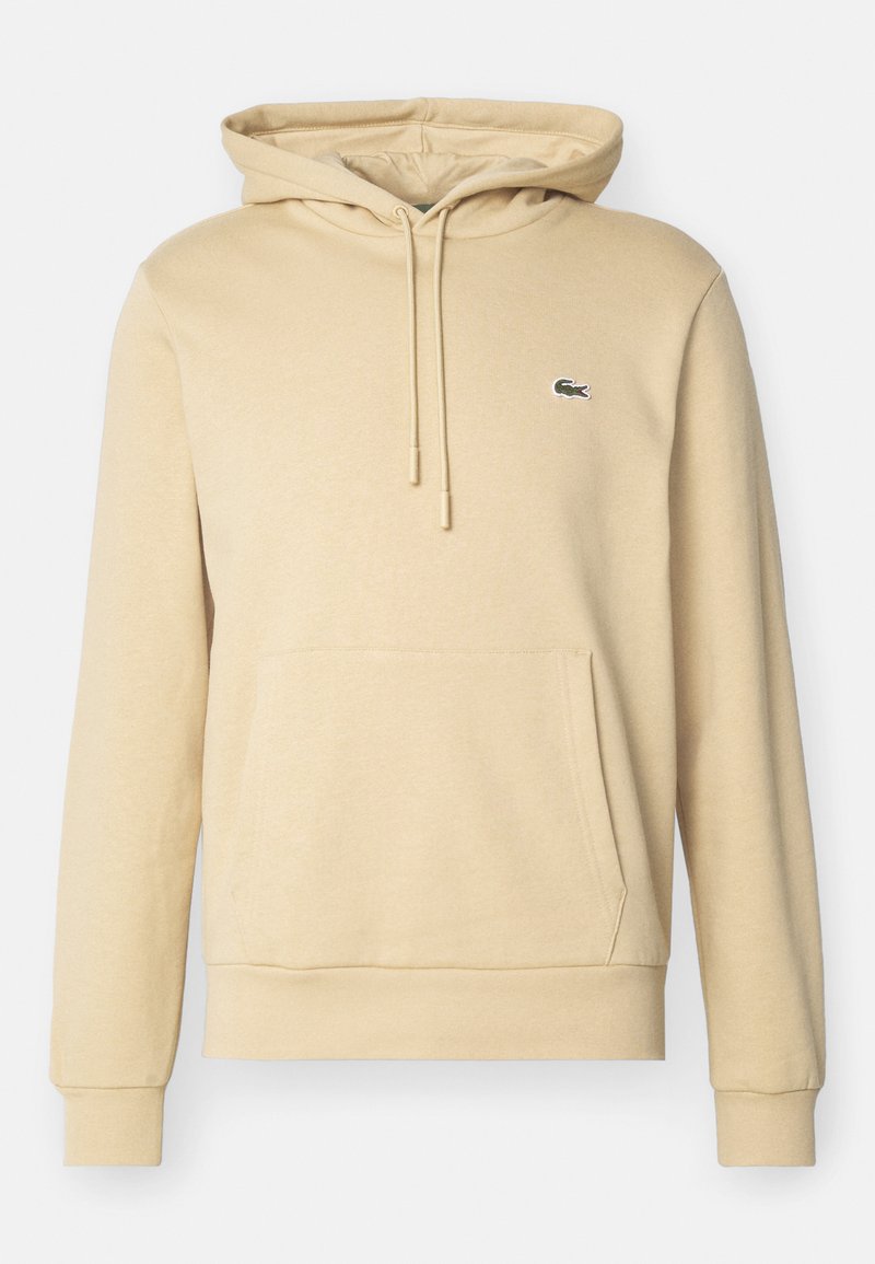 Beige Kapuzenpullover aus weichem Stoff, mit einer Känguru-Tasche, gerippten Bündchen und einem kleinen grünen Logo auf der Brust.