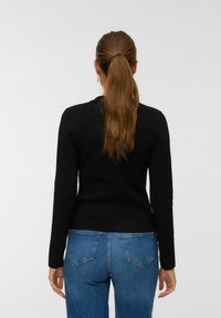 Svart långärmad topp med en figurnära design, rund hals och ribbad textur, i kombination med blå jeans med bakfickor.