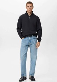 Zwarte zip-up sweater, lichtblauwe straight-leg jeans en zwarte schoenen. Soepele textuur op de sweater, klassieke denimstijl op de broek.