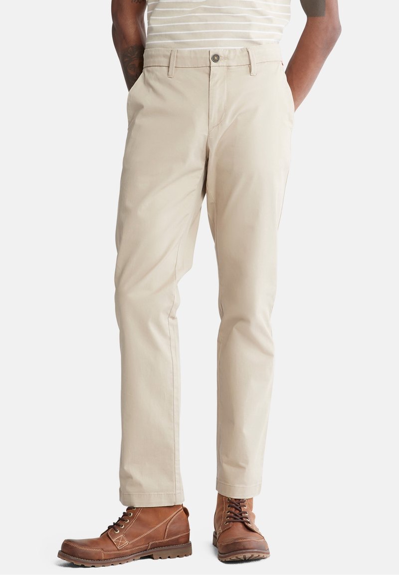 Beige chinos med rak bendesign och sidofickor. Bärs med bruna snörstövlar med kontrasterande sömmar och gummisulor.