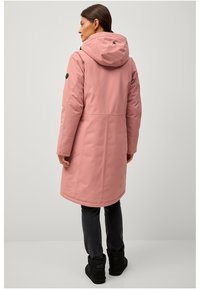 Roze waterdichte parka met een capuchon, voorzien van een gladde textuur, verstelbare trekkoorden en een zwart rond logo op de mouw.