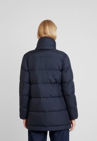 Chaqueta de plumón azul marino con cuello alto, diseño acolchado y mangas largas. Tela texturizada y un ajuste relajado que se extiende hasta las caderas.