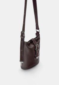 Braune Leder-Schultertasche mit silbernen Beschlägen, verstellbarem Riemen und einer Seitentasche. Glatte Textur mit weißen Nähakzenten.