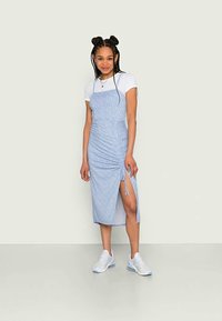 Vestido azul claro, estampado, com laterais franzidas e uma fenda alta até a coxa, sobreposto a uma t-shirt branca. Usado com tênis brancos.