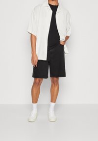 Košile s krátkým rukávem bílá košile přes černé tričko, doplněná černými džínovými šortkami a bílými teniskami s kotníkovými ponožkami.