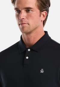 Marineblauw polo shirt gemaakt van katoen, met een klassieke kraag, drieknoopsluiting en een klein geborduurd pinguïnlogo op de linkerkant van de borst.