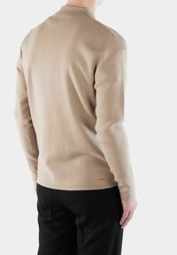 Beige langärmliger Strickpullover mit einer dezenten Textur und einem Kragen, ausgestattet mit einem kleinen roten Logoakzent am Saum. Taillierter Schnitt.