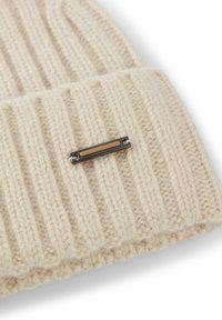 Beige strikket hue med ribbet tekstur og en metallisk detalje. Har en simpel bjælke med en lys brun midte indarbejdet i strikken.