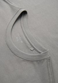 T-shirt en coton gris clair avec col rond, coutures visibles et étiquette de la marque imprimée à l'intérieur du col.