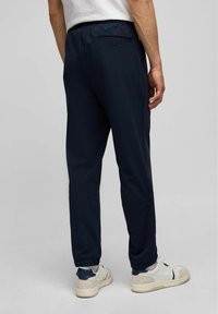 Mariene sportbroek met een getailleerde pasvorm, elastische tailleband en een achterzak met een knoopdetail. Gladde textuur en lichtgewicht materiaal.