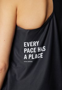 Débardeur de sport sans manches noir avec texte blanc : "CHAQUE RYTHME A SA PLACE" et "ADIDAS RUNNERS" au dos. Tissu lisse et léger.