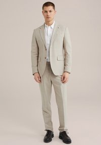 Beige karierter Anzug mit einer taillierten Passform, einreihigem Blazer und passender Hose. Kombiniert mit einem weißen Hemd und schwarzen Schuhen.