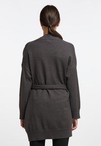 Mörkgrå oversized cardigan med bälte i midjan, ribbade manschetter och en mysig stickad textur. Exponerade sömmar förstärker designen.